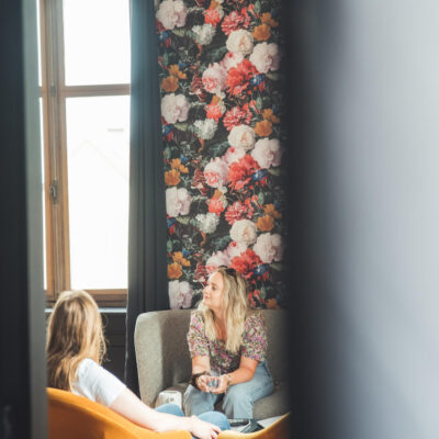 Deux femmes discutent dans un salon fleuri.