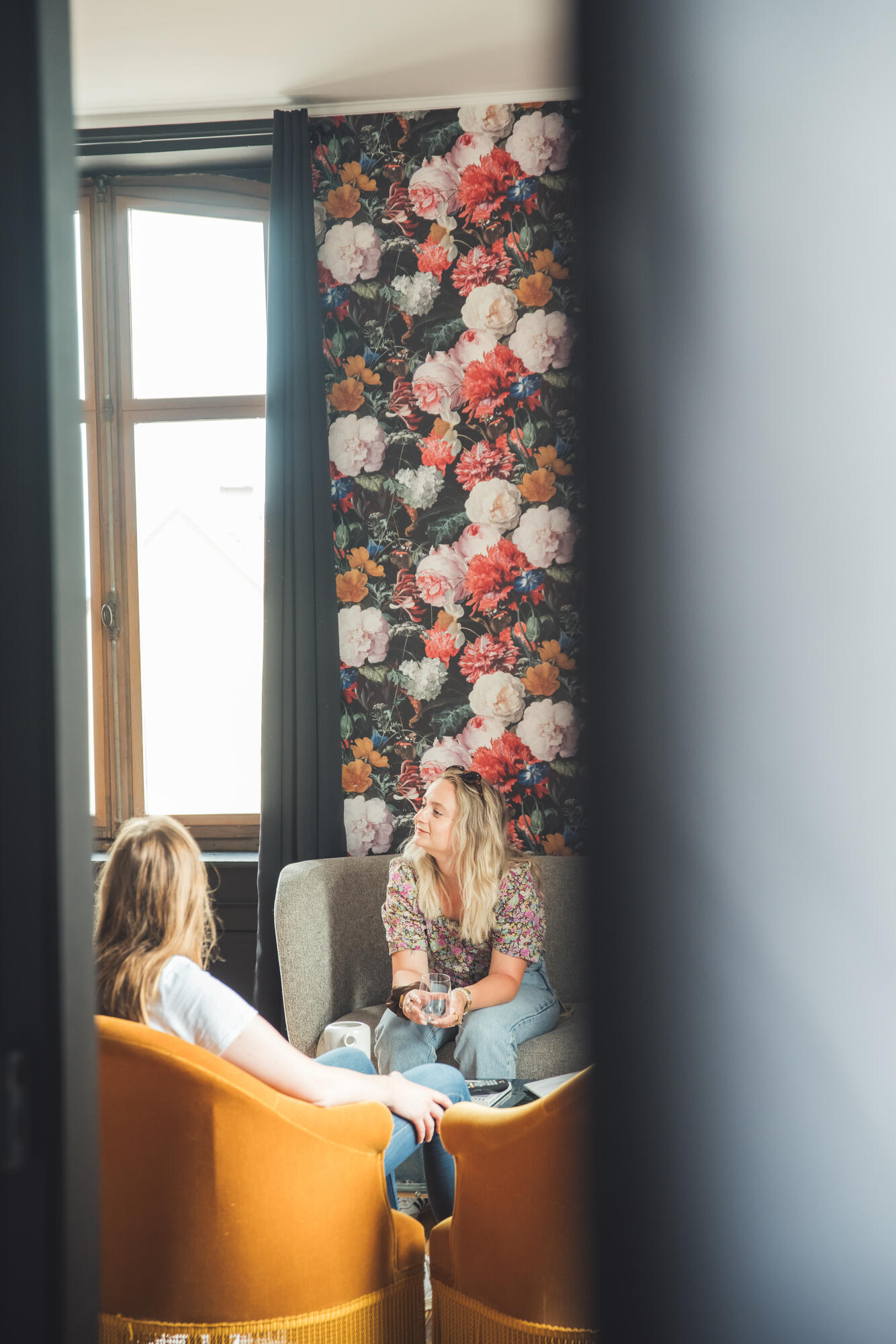 Deux femmes discutent dans un salon fleuri.